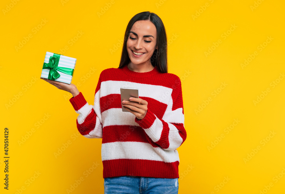 Close up photo of a cute smiling young trendy woman with gift box in hand isolated on yellow background Close up photo of a cute smiling young trendy woman with gift box in hand isolated on yellow background