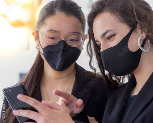 Dos mujeres de negocios con mascarilla consultan teléfono móvil photo