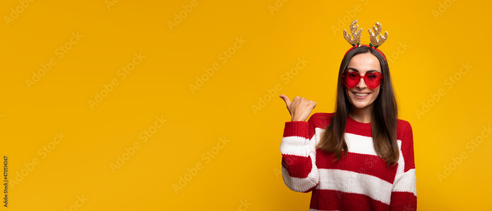 Banner wide photo of an attractive excited smiling young girl in Christmas reindeer antlers and sweater while she posing isolated on yellow background in studio - obrazy, fototapety, plakaty 
