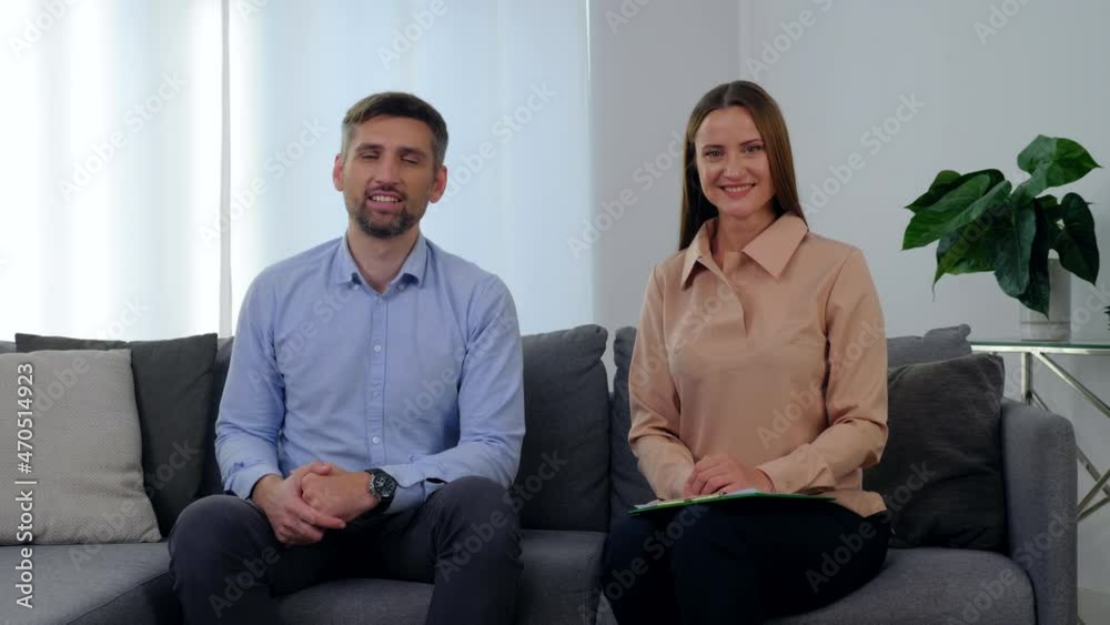 Portrait smiling woman psychologist and happy man patient sitting on couch in clinic office, looking camera after having passed positive psychotherapy session. Mental health problems after covid-19 Portrait smiling woman psychologist and happy man patient sitting on couch in clinic office, looking camera after having passed positive psychotherapy session. Mental health problems after covid-19
