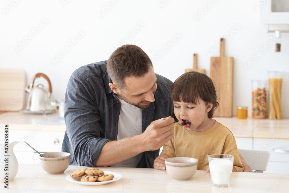 Kids nutrition. Loving daddy feeding his little son with porridge at kitchen in morning, man taking care about his child
