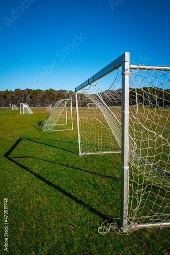 Soccer goal in the green field on blue sky background, a diagonal side view.