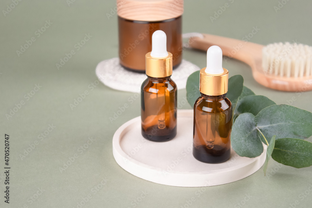 Glass dropper bottles and jars with natural organic cosmetics, natural bristles face or body dry brush - eucalyptus oil, face or body cream, essential oils on green background with copy space. Mockup