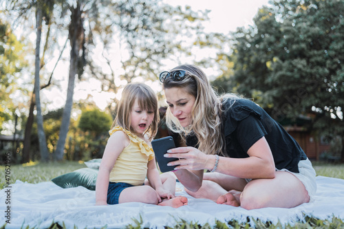 Young mother sharing smartphone with adorable little daughter in nature