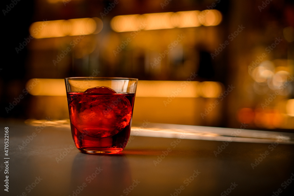 selective focus of transparent glass of cocktail with piece of ice stands on a bar counter