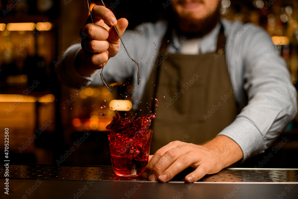 selective focus on glass in which bartender hand threw an ice cube and splashes of liquid scatter around