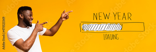 Positive African American guy pointing both hands aside at New Year loading progress bar over orange background photo