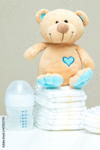 Stack of diapers with toy teddy bear and bottle of milk. set for boy girl for baby shower, copy space