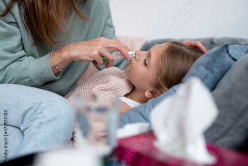 Mother sprays nasal medication into the nose of her ill daughter.