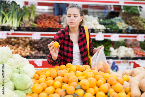 Fotografi Portrait of a concentrated young woman shopper near counter, puts tangerines in