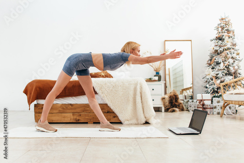 Young woman practicing at home bending forward with her arms outstretched.