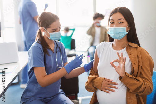 Vaccinated Pregnant Asian Lady Gesturing Okay Sign At Clinic