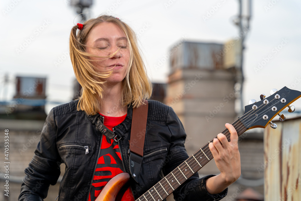 Young rock blonde girl with two funny ponytails, closed eyes , playing an  electric guitar on the roof of an old building, front view. Musical video  clip shooting. Outdoor show. Stock Photo |