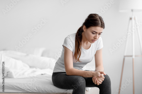 Despaired unhappy european young woman suffering from depression and sitting in bed at home