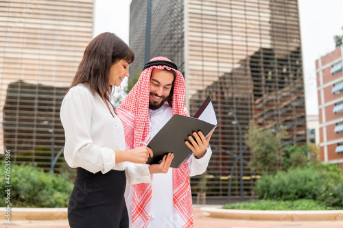 Happy arab man signing contract after negotiation with caucasian businesswoman at outdoor meeting