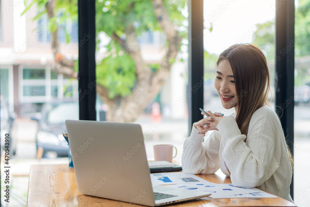 Asian businesswoman working with marketing graphs and laptop in online working concept with financial documents and analytical calculator while sitting in the office. Asian businesswoman working with marketing graphs and laptop in online working concept with financial documents and analytical calculator while sitting in the office.