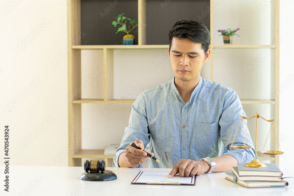 Fototapeta premium Asian male lawyer working on legal contract documents in a courtroom of justice. and legal concepts In the office with hammers and scales on the table