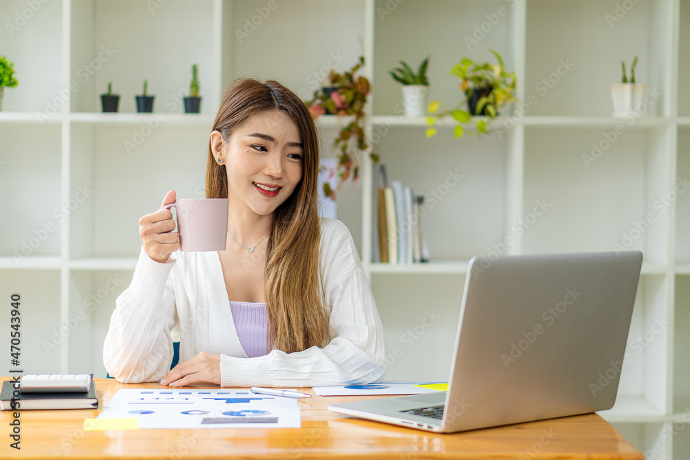 Asian businesswoman working with marketing graphs and laptop in online working concept with financial documents and analytical calculator while sitting in the office. Asian businesswoman working with marketing graphs and laptop in online working concept with financial documents and analytical calculator while sitting in the office.