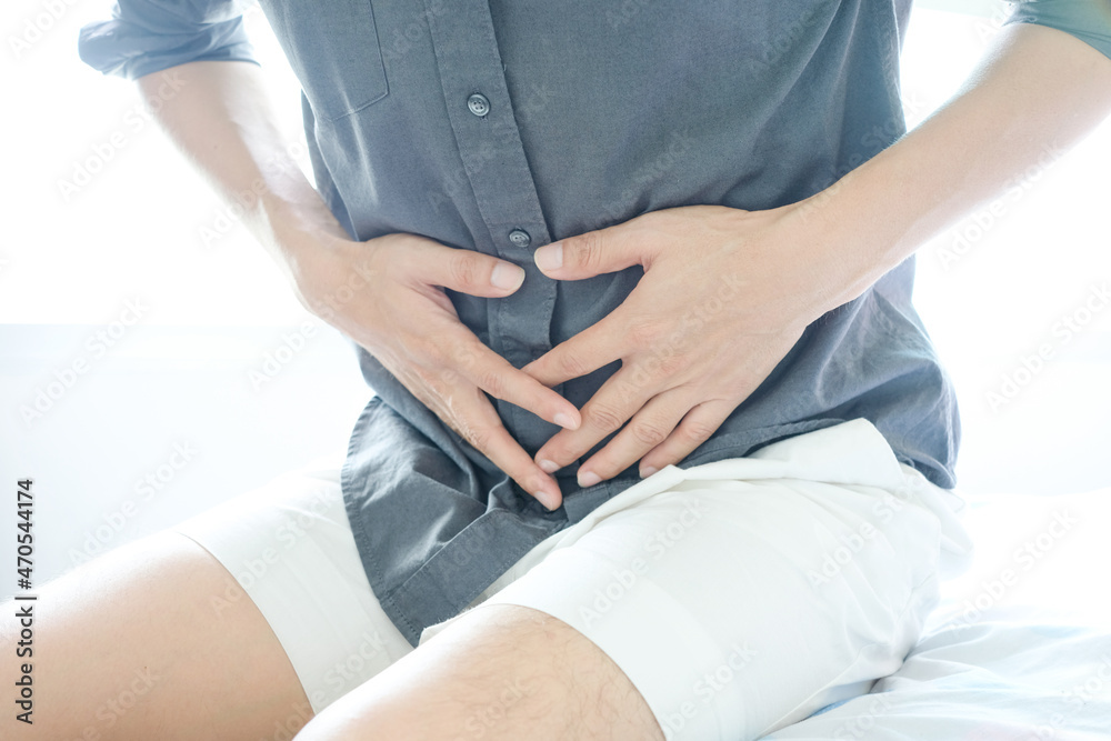 Young man uses his hands to hold his stomach and has a severe stomachache.