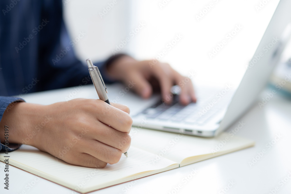 Closeup hand of business man writing on note while using laptop computer on desk at home, male planning on note for business success, author and blog, businessman working on table, employee and job. Closeup hand of business man writing on note while using laptop computer on desk at home, male planning on note for business success, author and blog, businessman working on table, employee and job.