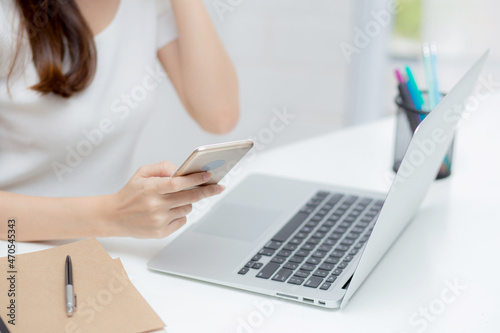 Closeup hand of young woman working laptop computer and reading smartphone on internet online on desk at home  freelance girl using phone with social media  business and communication concept.