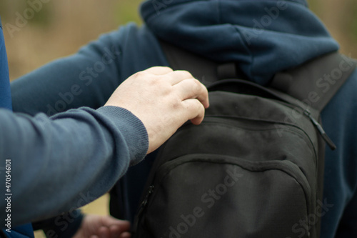 The guy is in a backpack. A man takes things from a friend's bag.
