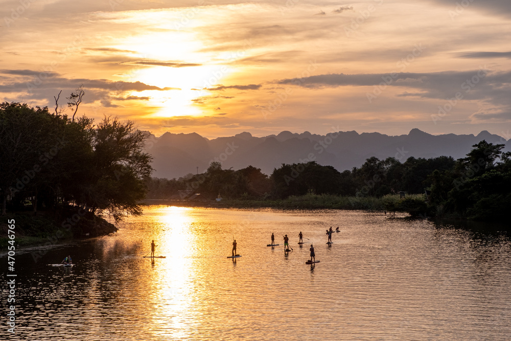 Stand-up paddleboarders in the River Kwai in Thailand at sunset