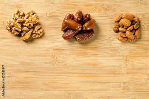 Raw almonds, organic pitted dates and walnut halves on the wooden cutting board background
