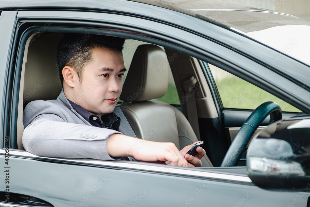 Happy businessman using smartphone calling while driving the car on his morning commute to work. Handsome Asian young man touching mobile phone communication on his luxury automobile on the road trip. Happy businessman using smartphone calling while driving the car on his morning commute to work. Handsome Asian young man touching mobile phone communication on his luxury automobile on the road trip.