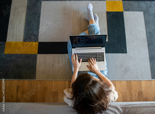 View from above of woman working on a laptop while sitting on the floor.
