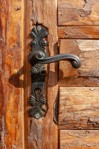 Vintage curly wrought iron handle on wooden door. Vertical photo.
