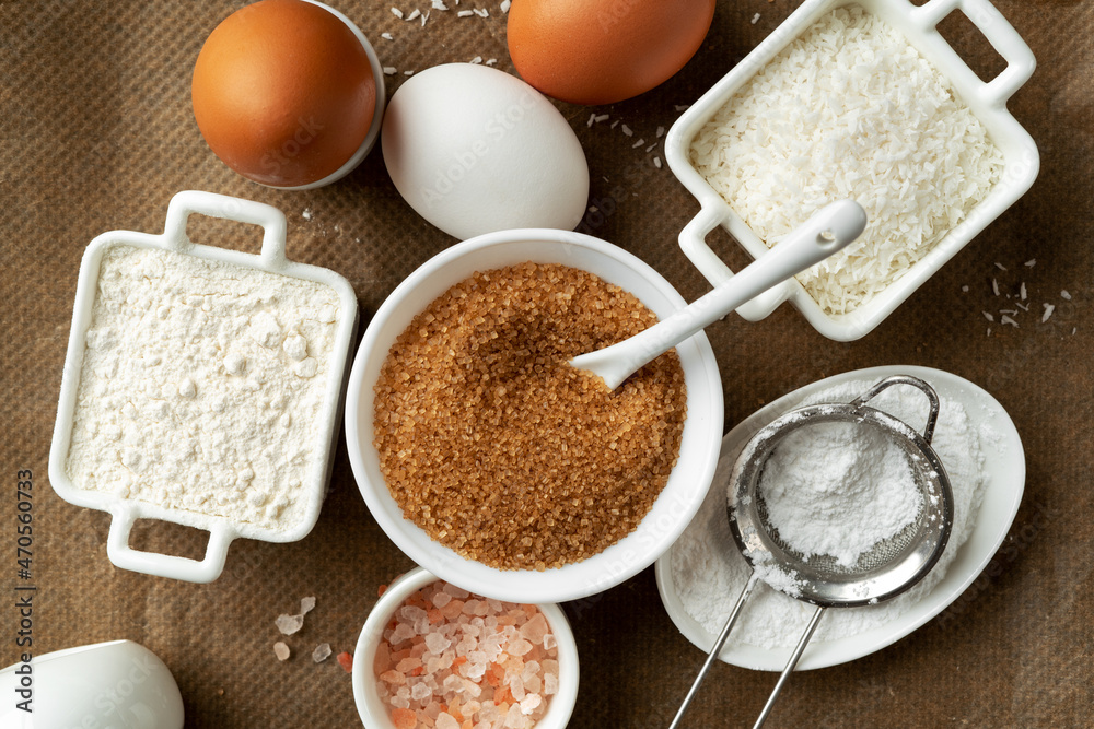Ingredients for coconut cookies or sweet pastries on a culinary background. Eggs, coconut chips, flour, sugar and salt on a dark table. Top view