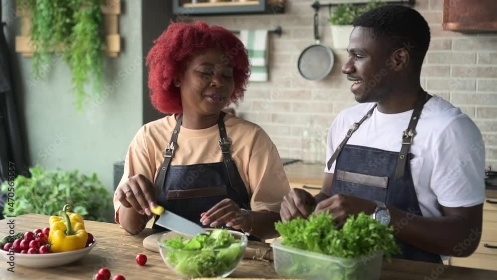 Young woman, man cooking salad and laughing while standing at table in home kitchen spbd. Beautiful African female, guy cut fresh vegetables and talk with happy smiles, laugh and stand at desk in Young woman, man cooking salad and laughing while standing at table in home kitchen spbd. Beautiful African female, guy cut fresh vegetables and talk with happy smiles, laugh and stand at desk in
