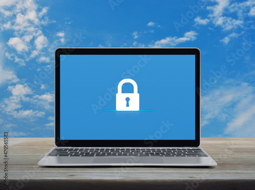 Padlock flat icon on modern laptop computer monitor screen on wooden table over blue sky with white clouds, Technology internet cyber security and safety online concept