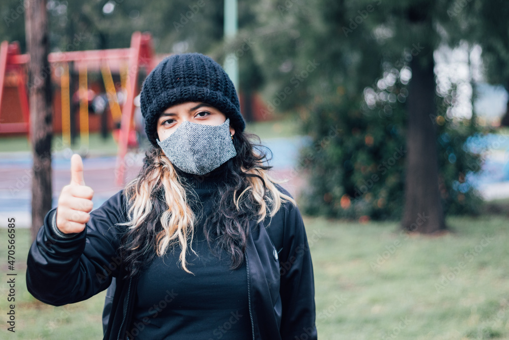Latin teenager college girl thumbs up standing at the park with face mask on Latin teenager college girl thumbs up standing at the park with face mask on