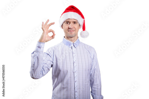 An adult confident man looks into the camera, the gesture is okay, everything is fine, dressed in everyday clothes, a light plaid shirt, a New Year's cap. Isolated, homogeneous background