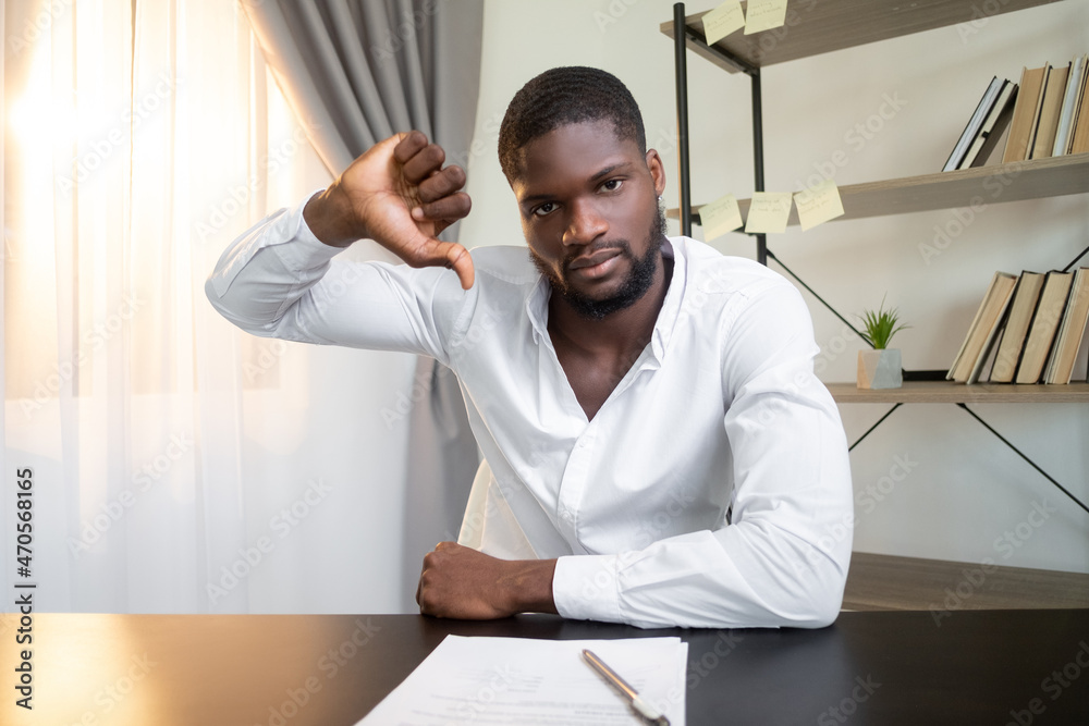 Fototapeta premium Contract reject. Offer disapproval. Project failure. Dissatisfied frown business man refusing deal with thumb down bad gesture at office workplace interior.