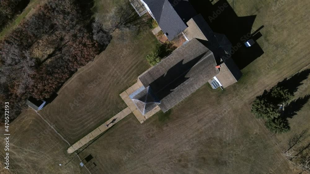 Top-down aerial view in 4k of a person walking along narrow paved path and going to church. 90 degree angle above old heritage building from the early 20th century in Spring Lake, Alberta. Top-down aerial view in 4k of a person walking along narrow paved path and going to church. 90 degree angle above old heritage building from the early 20th century in Spring Lake, Alberta.
