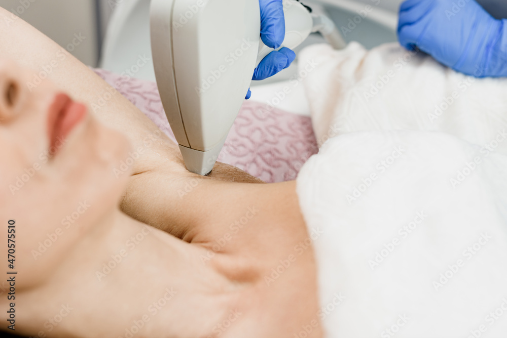 Fototapeta premium Young woman having underarm laser epilation in modern beauty salon
