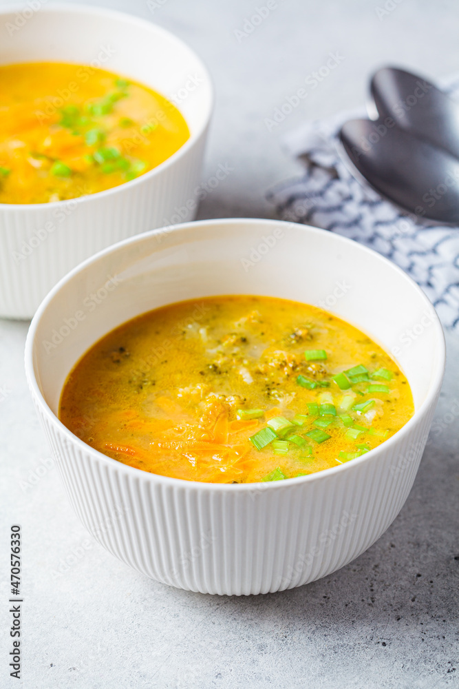 Homemade broccoli cheddar cheese soup with green onions in white bowl, gray background. Vegetarian food concept.