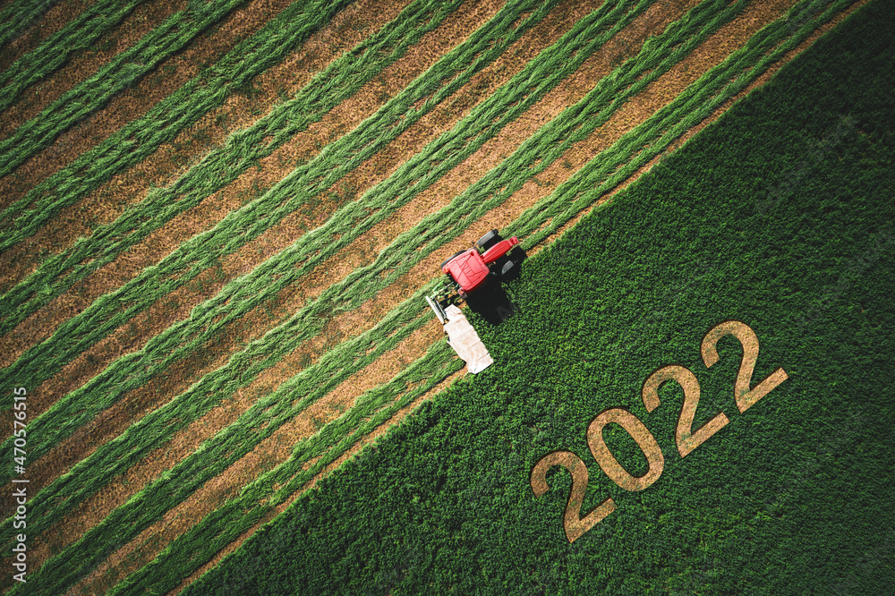 2022 Happy New year concept and red tractor mowing green field - obrazy, fototapety, plakaty 