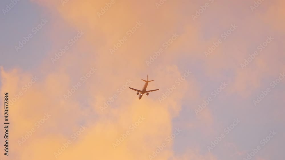 Commercial jet airplane flying high in cloudy sky during golden hour. View from ground. Wing vapor condensation clouds. Commercial jet airplane flying high in cloudy sky during golden hour. View from ground. Wing vapor condensation clouds.