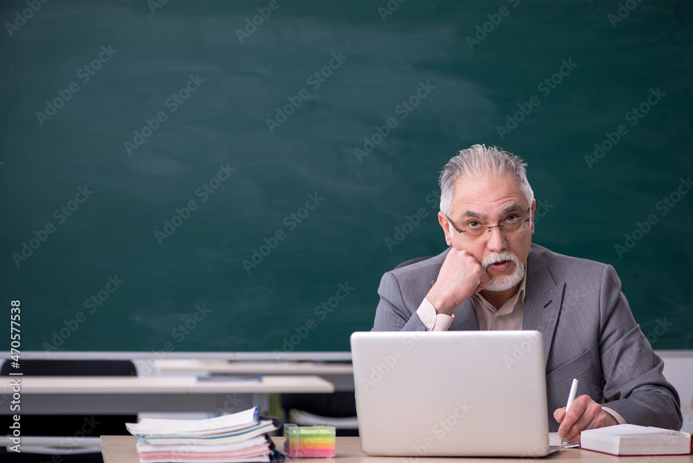 Old male teacher in front of blackboard Old male teacher in front of blackboard