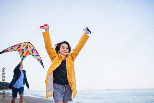 Low angle view of preteen girl and her grandfather playing with kite on sandy beach.