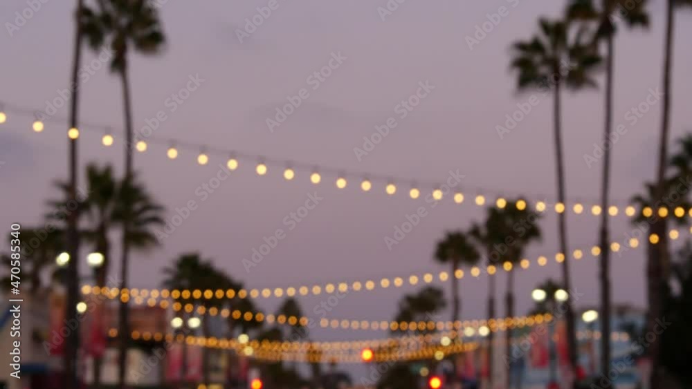 Defocused illuminated electric garland, palm trees silhouettes, Oceanside California USA. Ocean beach tropical pink sunset, pacific coast purple twilight sky. Los Angeles vibes. Bulb lights glowing.