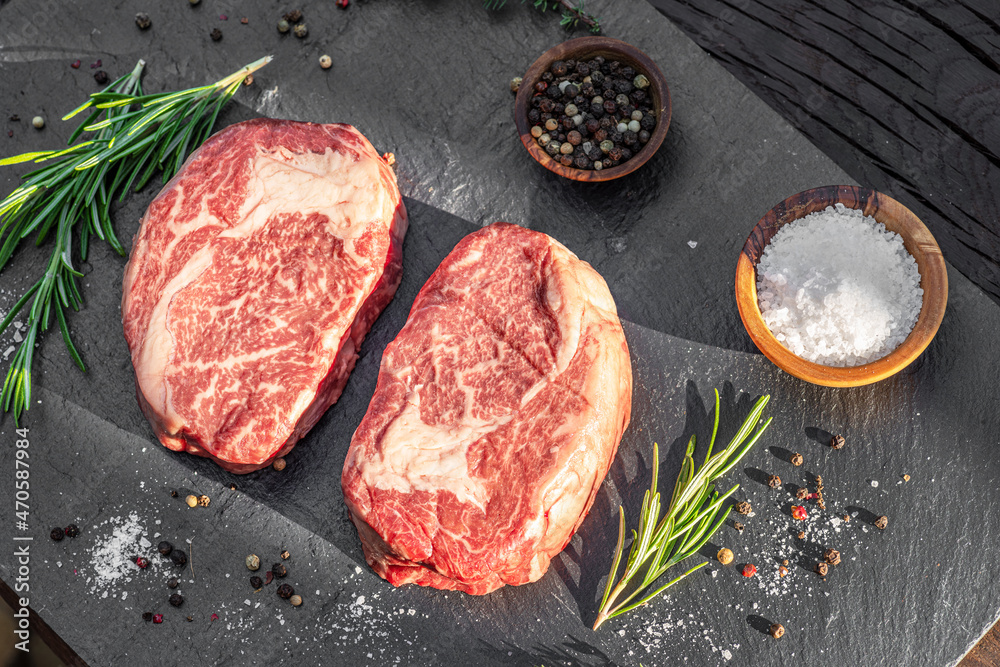 Raw Ribeye steaks with salt and herbs on grey board. Top view.