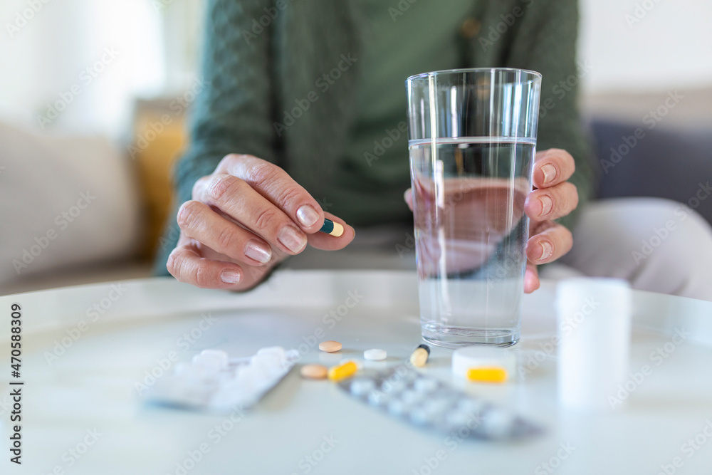 Healthcare concept. Cropped view of senior woman take vitamin pill, holding cup with water in hands, sitting alone behind wooden table Healthcare concept. Cropped view of senior woman take vitamin pill, holding cup with water in hands, sitting alone behind wooden table