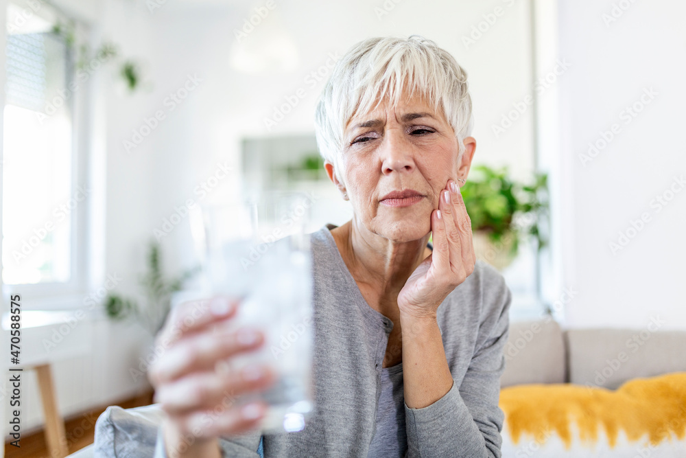 Senior woman with sensitive teeth and hand holding glass of cold water with ice. Healthcare concept. Mature woman drinking cold drink, glass full of ice cubes and feels toothache, pain Senior woman with sensitive teeth and hand holding glass of cold water with ice. Healthcare concept. Mature woman drinking cold drink, glass full of ice cubes and feels toothache, pain