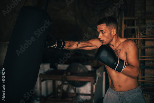 Shirtless young athlete practicing boxing with punching bag at home gym photo