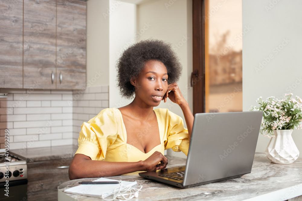 Portrait of beautiful African American freelancer woman, table in kitchen. Work on laptop, indoor. Portrait of beautiful African American freelancer woman, table in kitchen. Work on laptop, indoor.